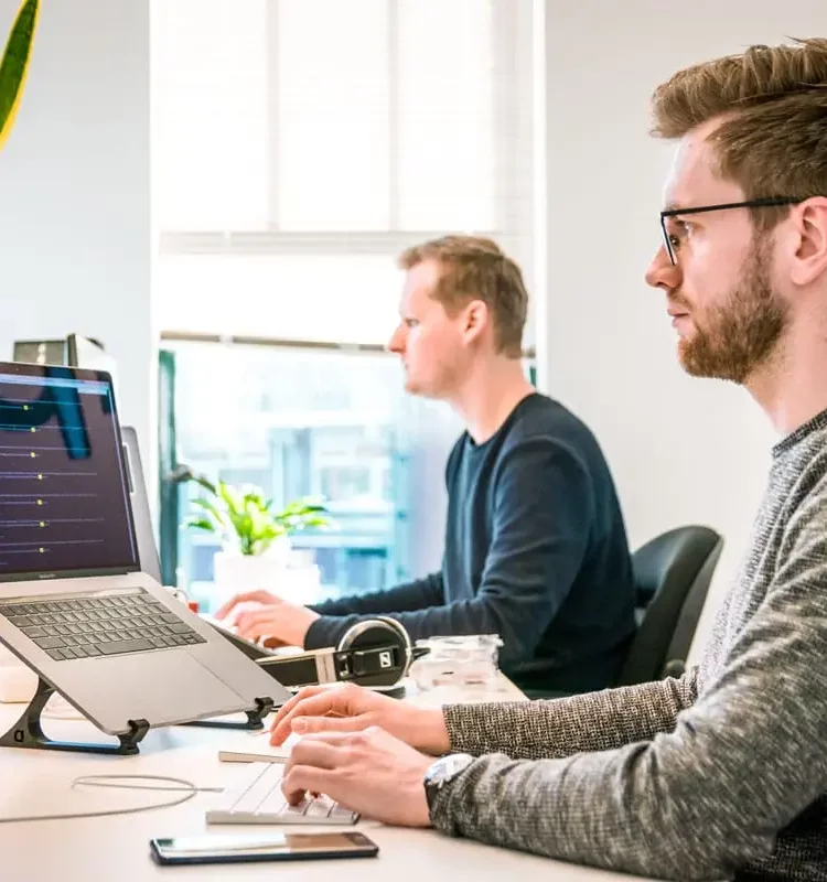 Zwei IT-Spezialisten arbeiten im Büro an Computersystemen und überwachen sicherheitsrelevante Prozesse